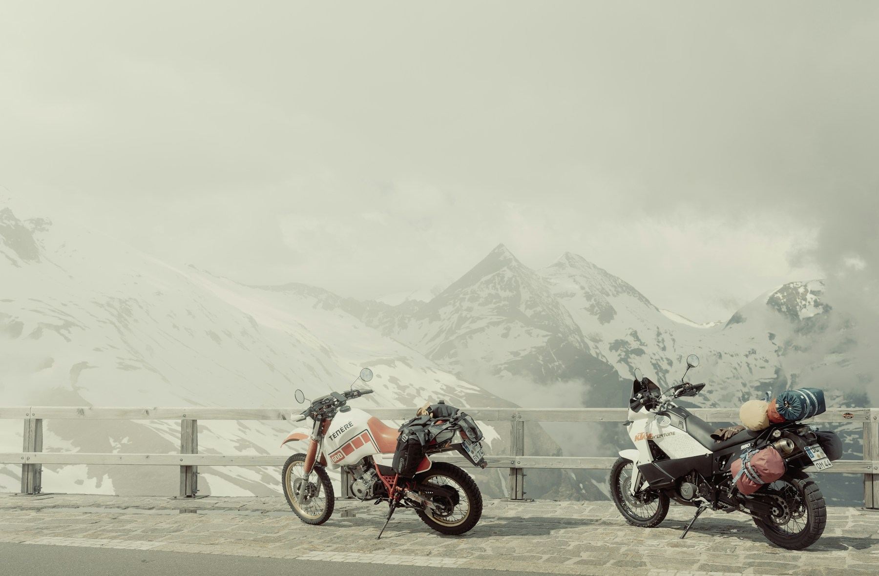 Two loaded motorcycles stopped below snowy Austrian mountains